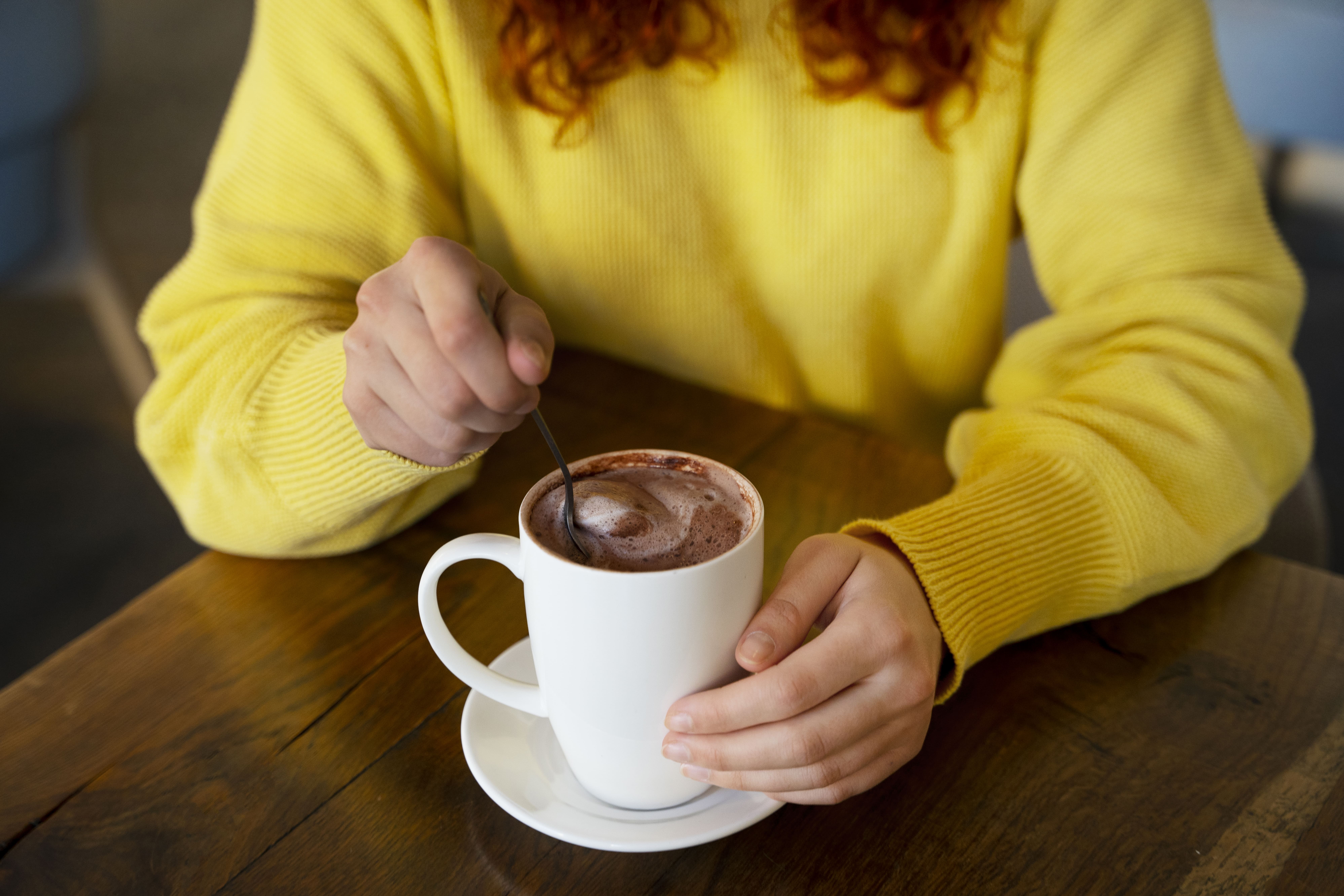 Persona con suéter amarillo revolviendo una taza de chocolate caliente