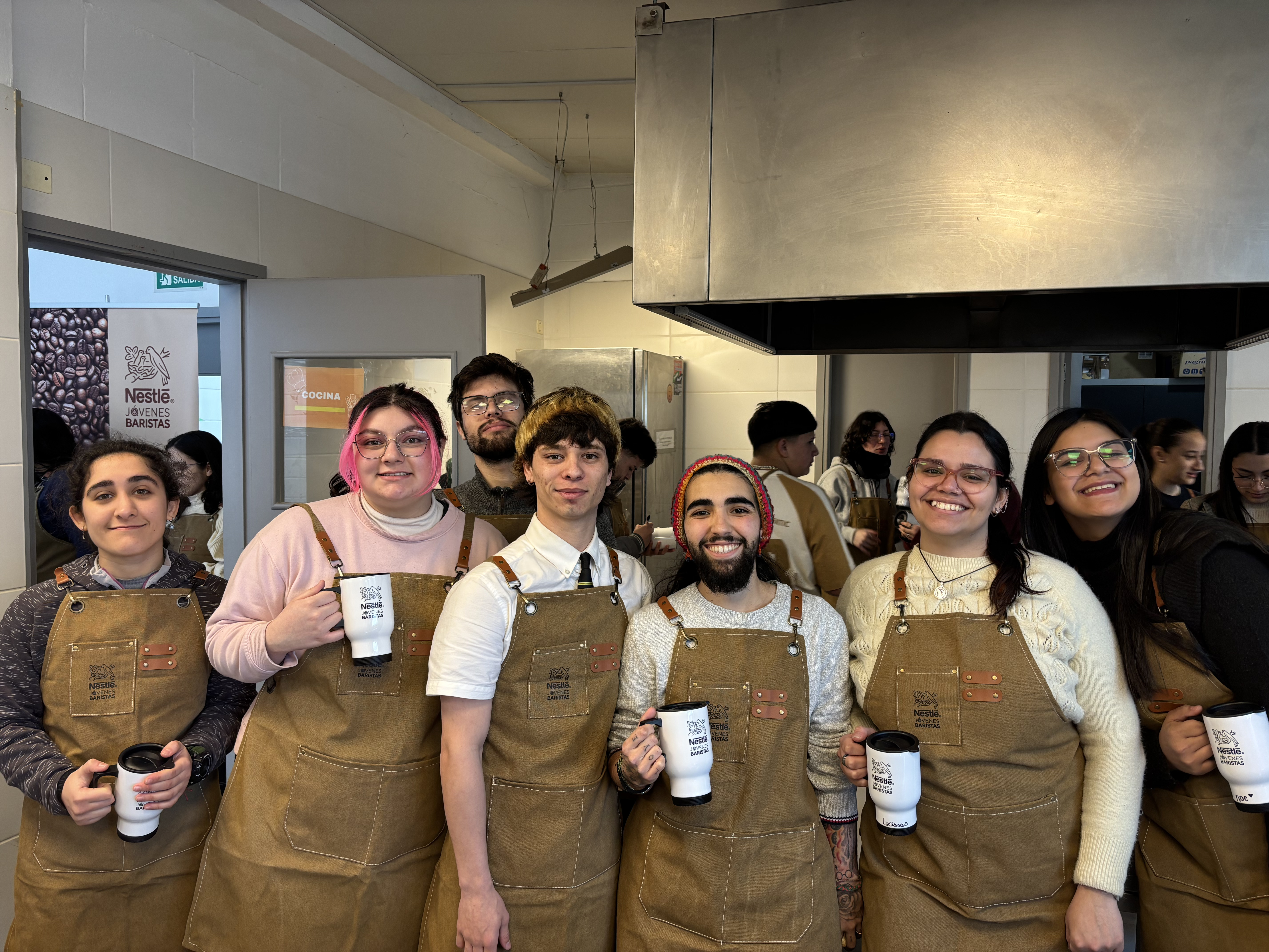 Participantes de Nestlé Jóvenes Baristas posan con sus delantales en una cocina